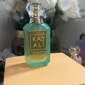 Kayali Maui in a Bottle Sweet Banana - 10ml. Kayali Maui in a Bottle Sweet Banana 37 är en parfym i en snygg, grön glasflaska med guldiga detaljer och en kristalliknande kork. Flaskan har en modern, kantig form och etiketten är stilren med vit text. Doften har tropiska och fruktiga vibbar med banan som huvudnot.