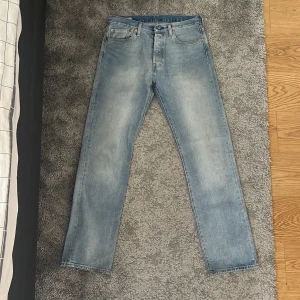 Levi's 501 ljusblå jeans W32 L34 - Säljer ett par klassiska Levi's 501 Premium jeans i ljusblå tvätt. Modellen har rak passform, fem fickor och knappgylf. Jeansen är tillverkade i slitstarkt bomullsmaterial och har den ikoniska läderpatchen bak i midjan. Perfekt för dig som gillar tidlös och clean stil.