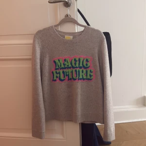 Grå stickad tröja från From Future - Grå stickad tröja från From Future med coolt broderat tryck i grönt, blått och rosa som säger 'MAGIC FUTURE' på bröstet. Rund hals, ribbade muddar och långärmad. Perfekt för dig som gillar statement-plagg och mjuka material.