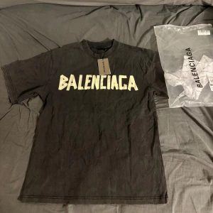 Svart Balenciaga t-shirt med tryck - Cool svart t-shirt från Balenciaga med stort vitt tryck på bröstet och gul grafisk logga på ryggen. Oversized passform och klassisk rund hals. Materialet är mjuk bomull och t-shirten har korta ärmar. Perfekt statement-plagg för dig som gillar streetwear.