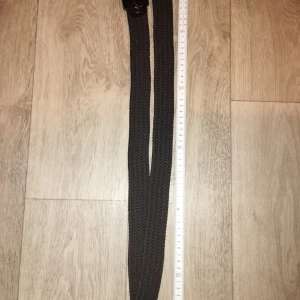 Svart flätad bälte med metallspänne - Snyggt svart bälte med flätad design och ett stilrent svart metallspänne. Bältet är flexibelt och har en modern look som passar till jeans eller chinos. Materialet är syntet och spännet ger en cool touch till outfiten.