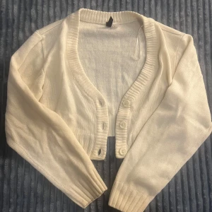Vit croppad kofta 🤍 - Säljer en vit croppad kofta från H&M Divided, strl XS. Koftan har ribbade muddar, v-ringad hals och knappar framtill. Den är stickad i mjukt material och har långa ärmar. 🥰 Säljer endast p.g.a den inte passar mig längre, och inte heller används något mer.