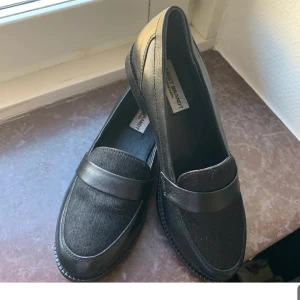 Svarta loafers från Margit Brandt - Snygga svarta loafers från Margit Brandt med rund tå och platt sula. Skorna har en stilren design med en bred rem över foten och är tillverkade i skinn med en lätt hårig finish på ovansidan. Perfekta för dig som gillar klassisk och clean stil. Aldrig använda. Skinn