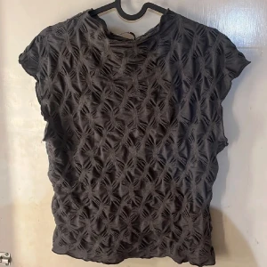 Svart topp  - Unik svart topp  med quiltad struktur och korta ärmar. Mönstret ger en riktigt snygg 3D-effekt och gör toppen till ett statement-plagg. Perfekt för dig som vill sticka ut med en annorlunda stil. Passar till både jeans och kjol.