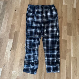 Svarta rutiga mjukisbyxor från 157 - Säljer ett par svarta och vita rutiga mjukisbyxor från 157, storlek L. Byxorna har elastisk midja med snörning och är gjorda i mjukt bomullsmaterial. Perfekta för chill dagar hemma eller när du vill vara extra bekväm.