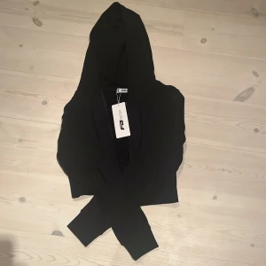 Svart hoodie från FB Sister, M -  En kort Svart hoodie från FB Sister i storlek M. Tröjan har en klassisk huva och långa ärmar, med en enkel och clean look. Materialet är mjukt och skönt, perfekt för chill dagar. Dragkedja framtill gör den enkel att ta på och av. Snygg basic som funkar till det mesta.
