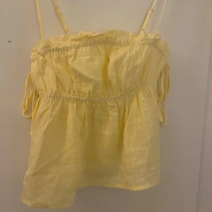 Ljusgul linnetopp från Nelly - Supersöt ljusgul linnetopp från Nelly med tunna axelband och volangdetaljer upptill. Toppen har knyt på sidorna och är tillverkad i ett luftigt linnematerial som ger en chill och flowy vibe. Perfekt för soliga dagar och sommarhäng!