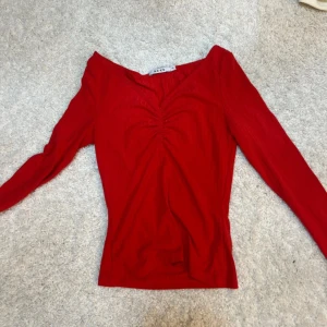 Röd omlottopp från NA-KD -  röd omlottopp från NA-KD med lång ärm och v-ringad hals. Toppen har en rynkad detalj framtill och är gjord i mjuk ribbad bomull. .