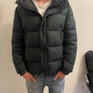 Svart dun/pufferrjacka från BOSS - Säljer en svart pufferjacka från BOSS med huva och snygga knappar framtill. Jackan är i moddelen Omaris, storlek M men passar större och mindre.