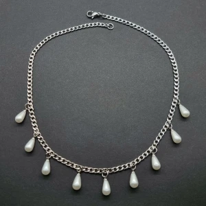 Silverhalsband med droppformade pärlor - Stilrent halsband i silverfärgad kedja med sju droppformade vita pärlor som hänger längs hela kedjan. Kedjan har en klassisk länkkonstruktion och pärlorna ger en cool och elegant vibe. Perfekt för dig som vill sticka ut med något unikt och trendigt.