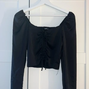 Svart långärmad topp från Bik Bok - Trendig svart topp från Bik Bok i storlek XS med långa puffärmar och croppad passform. Toppen har smockad rygg, snörning framtill och lätt glansigt tyg. Perfekt för dig som gillar en stilren men ändå cool look. Priset kan diskuteras 