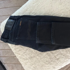 Svarta jeans från Nudie Jeans  - Snygga svarta jeans från Nudie Jeans med klassisk femficksdesign och diskret logga på bakfickan. Modellen är skinny med smal passform och raka ben. Jeansen är tillverkade i mjukt bomullsmaterial med stretch för extra komfort. Skick- 9/10. Byxorna är knappt använda och tvättas innan leverans. Om priset inte passar dig kan vi diskutera priset.