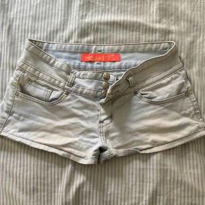 Ljusblå lågmidjade jeansshorts - Snygga ljusblå jeansshorts från Just for You med lågmidja och tre knappar framtill. Klassisk femficksdesign och bälteshällor. Perfekta för varma dagar och har en fräsch, modern look som passar till allt. Materialet är mjukt denim och färgen är ljusblå.