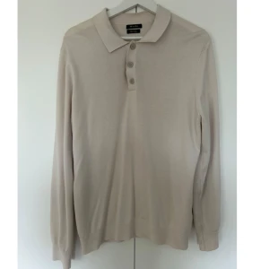 Beige långärmad pikétröja Massimo Dutti - Snygg beige pikétröja från Massimo Dutti med klassisk krage och tre knappar framtill. Tröjan är långärmad och har en mjuk, tunn känsla som passar perfekt för dig som gillar stilrena och enkla plagg. Perfekt att matcha med jeans eller chinos.