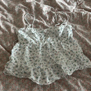 Blommig volangtop med smala axelband - Supersöt blommig topp med volanger och smala axelband.