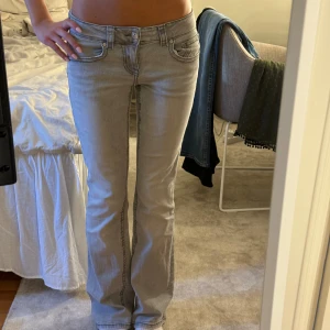Grå lågmidjade bootcut jeans  - Snygga ljusgrå jeans med bootcut från Gina. Jeansen har låg midja och knappar på bakfickorna. Storlek 38 men passar mig perfekt som har 32/34
