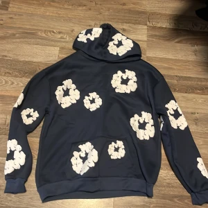 Blå hoodie, Denim Tears - Säljer en blå hoodie från Denim Tears. Hoodien har huva, känguruficka och är långärmad. Perfekt för dig som vill sticka ut med en unik och trendig stil. Aldrig använd.