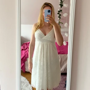 Vit spetsklänning med rosett - Superfin vit kortklänning i spets med smala axelband och v-ringning. Band vid midjan som man knyter till en fin rosett. Aningen missfärgad i armhålorna. Står ingen storlek, men skulle tro att den passar dig som har strl 36-40.