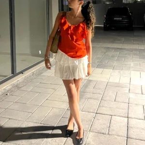 Röd volangtop med smala axelband - Snygg röd linnetopp med smala axelband och volangdetaljer framtill. Toppen har en v-ringad form och är ärmlös, perfekt för varma dagar. Materialet känns lätt och luftigt, vilket gör den superbekväm att bära.