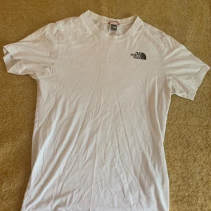 Vit t-shirt från The North Face XS  - 🚨Pris kan diskuteras🚨Snygg vit t-shirt från The North Face i storlek XS. Framsidan har en liten svart logga på bröstet och baksidan har en stor röd fyrkant med logga och texten 'Never Stop Exploring'. Tillverkad i mjuk bomull och har klassisk passform med korta ärmar.