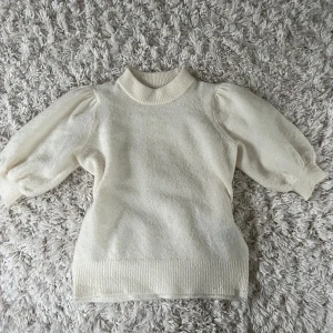 Vit stickad tröja med puffärm från ONLY - Superfin vit stickad tröja från ONLY med puffiga trekvartsärmar och ribbade muddar. Hög ribbad halsringning och mjukt material som känns skönt mot huden. Perfekt för lager-på-lager och snygg till både jeans och kjol.