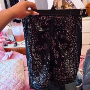 Svarta paisley-mönstrade shorts FBsister - Svarta shorts från FBsister i storlek XS med vitt paisley-mönster och snörning framtill. Modellen är loose fit och har en liten slits på båda  sidan för extra vibe. Perfekta för dig som gillar streetstyle och vill sticka ut med coola detaljer.