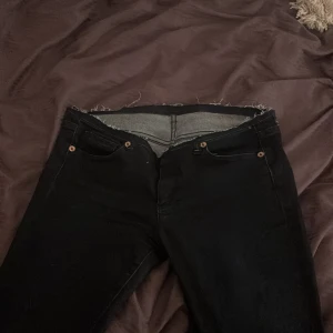 Svarta ultra low waits bootcut jeans med rå kant - Svarta jeans med bootcut passform och rå, fransig midja för en edgy vibe. Klassisk femficksmodell med svarta bakfickor och kopparfärgade nitar. Jeansen är i ett stretchigt denimtyg som sitter snyggt och bekvämt.