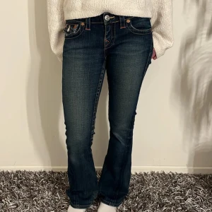 True Religion Joey bootcut jeans blå - Snygga True Religion Joey jeans i mörkblå tvätt med kontrastsömmar och ikoniska bakfickor med lock och knappar. Bootcut-modell med låg midja och klassisk femficksdesign.  Defekt syns på de två sista bilderna men syns bara på utsidan, är inte ett hål igenom byxan. Byxorna har även ett skosnöre inuti pågrund av att kunna fixa hur tight de sitter!💓 !!PRIS KAN DISKUTERAS VID SNABB AFFÄR!! Mått: midja - 39cm