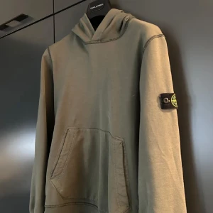 Olivgrön hoodie från Stone Island - Säljer ni en stilren grön hoodie från Stone Island. Tröjan har en klassisk design med huva och en magficka. Tröjan är Inhandlad på Nordiska Kompaniet för 2100 kr. Varan är i ett mycket bra skick utan befintliga defekter och är sparsamt använd. Hör gärna av er vid frågor eller funderingar så svarar jag gladligen! 