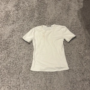 Vit t-shirt med spetsdetalj från Zara - Vit t-shirt från Zara i storlek M. T-shirten har korta ärmar med snygg vit och svart spetsdetalj vid ärmsluten. Materialet känns mjukt och stretchigt