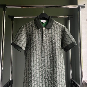 Lacoste monogram piké - Snygg grön pikétröja från Lacoste i klassisk passform. Tröjan har korta ärmar, krage och knappar framtill. Mönstret är geometriskt i vitt och grönt, och materialet känns som bomull. Perfekt för dig som gillar stilrena men unika plagg. Ny pris är 2000-1700kr, pris kan diskuteras!