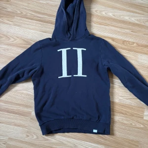 Mörkblå hoodie med stort II-tryck - Snygg mörkblå hoodie med stor vit II-logga på bröstet. Tröjan har huva och långa ärmar, samt ribbade muddar vid ärmslut och nederkant. Perfekt för dig som gillar en enkel men stilren look.