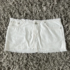 Snygg vit jeanskjol med fransar - Vit kort jeanskjol med fransad rå kant både upptill och nedtill. Kjolen har klassiska jeansfickor fram och bak samt knapp och dragkedja framtill. Perfekt för dig som gillar en clean och chill stil.