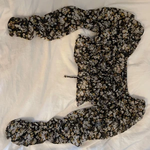Blommig croppad blus med snörning - Supersöt croppad blus från Gina Tricot med svart botten och blommigt mönster i vitt och gult. Långa puffiga ärmar och snygg snörning framtill. Supersnygga färger nu inför hösten🍂🍂 