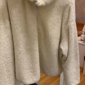 Beige fluffig hoodie med half zip - Supermjuk och fluffig beige hoodie med huva och half zip-dragkedja framtill. Perfekt för mysiga dagar och har en oversized känsla. Långärmad och tillverkad i gosig fleece som håller dig varm.