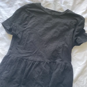 Svart kort klänning från SHEIN  - En svart blus från SHEIN i storlek XS. Klänningen har rund hals, korta ärmar och ett lätt rynkat parti vid midjan som ger en skön och avslappnad look. Tillverkad i mjuk bomull, perfekt för dig som gillar enkel och stilren design.