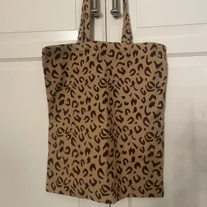 Leopardmönstrad tygpåse🐆  - Säljer en beige shoppingväska med brunt leopardmönster från ullared/gekås. Väskan har två långa handtag och är tillverkad i ett slitstarkt bomullstyg. Perfekt för att bära med sig allt man behöver under dagen och ger en cool touch till din outfit.