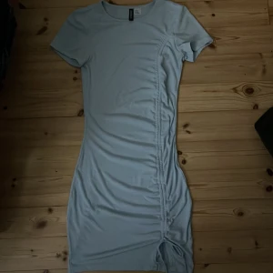 Ljusblå kortklänning med snörning - Säljer en ljusblå klänning från H&M med snörningsdetalj längs sidan som ger en snygg rynkad effekt. Klänningen har rund hals, korta ärmar och är gjord i mjukt och stretchigt material. Perfekt för dig som gillar enkel men trendig stil.
