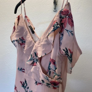 Ljusrosa blommig långklänning Rut&Circle - Superfin ljusrosa långklänning från Rut&Circle i storlek XS. Klänningen har tunna axelband, v-ringning och volangdetaljer vid axlarna. Blommigt mönster i rosa och grönt ger en romantisk vibe. Perfekt för sommarens alla tillfällen!
