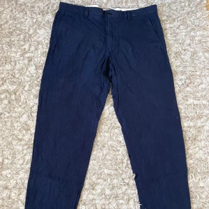 Marinblå linnebyxor från Zara - Snygga marinblå linnebyxor från Zara i rak modell med klassiska fickor fram och bak. Byxorna är tillverkade i 100% linne, vilket gör dem riktigt sköna och luftiga. Perfekta för dig som gillar stilrena och enkla plagg med en modern touch. En av Sömarna på baksidan av byxorna har spruckit, där av det billiga priset. Men det går lätt att laga och dem är annars i bra skick.