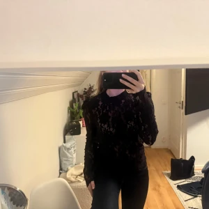 Svart spetsblus med puffärm - Säljer en svart blus i spets med lång ärm och puff vid axlarna. Blusen är genombruten och har en hög hals, vilket ger en riktigt snygg och trendig look. Perfekt att styla med jeans eller kjol för en cool outfit.
