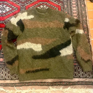 Camo stickad tröja från Valient - Säljer en fluffig och stickad tröja från Valient med camouflagemönster i grönt, brunt, svart och beige. Tröjan har rund halsringning och långa ärmar. Perfekt för dig som gillar streetwear och vill sticka ut med en unik look. Ny pris: 800