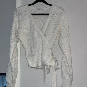 Vit omlottstickad kofta från NA-KD - Superfin vit stickad kofta från NA-KD med omlottmodell och knytband i midjan. Tröjan har långärmade ärmar och en mysig, lite luftig stickning. Perfekt att slänga på sig över ett linne eller t-shirt.