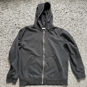 Svart hoodie med dragkedja - Svart Weekday hoodie med hel dragkedja och huva med snörning. Tröjan har två stora fickor framtill och ribbade muddar vid ärmslut och nederkant. 