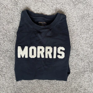 Mörkblå sweatshirt från Morris Gents - Snygg mörkblå sweatshirt från Morris Gents med stora vita bokstäver framtill. Klassisk rund halsringning och långa ärmar. Tillverkad i mjuk bomull, perfekt för en chill och stilren look.