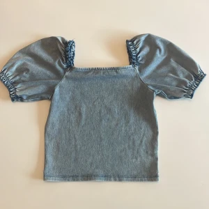 Jeansblå topp med puffärmar H&M - Superfin jeansblå💙🦋 topp från H&M med puffiga kortärmar och resår vid axlar och ärmslut. Toppen har en rak passform och är gjord i mjukt jeanstyg och som är perfekt till att styla med både kjol och jeans för en trendig look. Den sitter ganska tajt i är lite cropped på mig som är 165cm, men såååå snygg 😻 💋