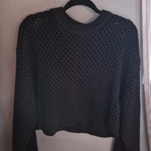 Svart stickad tröja Divided H&M - Svart stickad tröja från Divided H&M i storlek M. Tröjan har ett grovmaskigt, håligt mönster och ribbade muddar vid ärmslut och nederkant. Perfekt för lager-på-lager och ger en cool, avslappnad vibe.