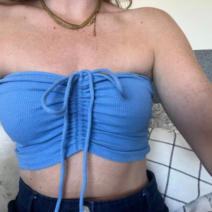 Blå ribbad bandeau tubtopp med snörning - Supersnygg blå bandeau tubtopp i ribbat material med justerbar snörning framtill. Toppen kan stylas på olika sätt, antingen med knyt runt halsen eller som klassisk bandeau. 