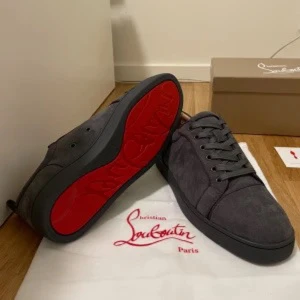 Grå mocka sneakers från Louboutin - Snygga grå sneakers från Christian Louboutin i mocka med klassisk röd sula. Skorna har rund tå, platt sula och ton-i-ton snörning. Perfekta för dig som vill ha en stilren men ändå lyxig look med den ikoniska röda undersidan.