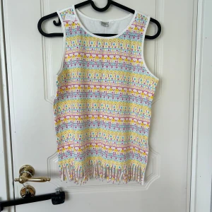 Färgglad fransad linnetopp LC Waikiki - Säljer en superfin ärmlös linnetopp från LC Waikiki med färgglatt geometriskt mönster i rosa, gul, blå och vit. Toppen har fransar längst ner som ger en cool och lekfull vibe. Perfekt för varma dagar och sommarhäng!